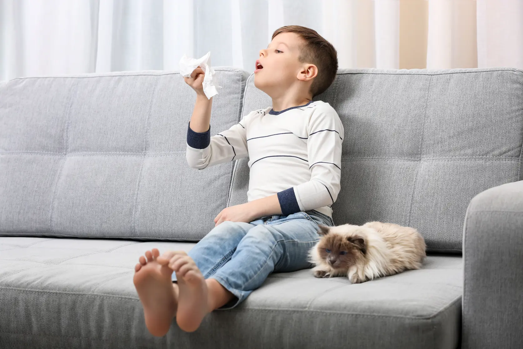 Bilde av en liten gutt som sitter i en sofa med en hund ved siden av seg og nyser
