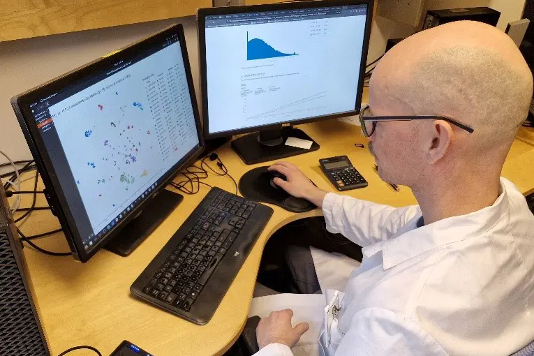 En mann som sitter ved et skrivebord med en datamaskin og en telefon