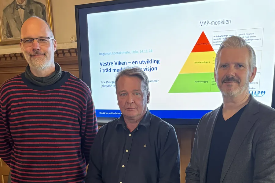 En gruppe menn som poserer for et bilde foran en stor skjerm